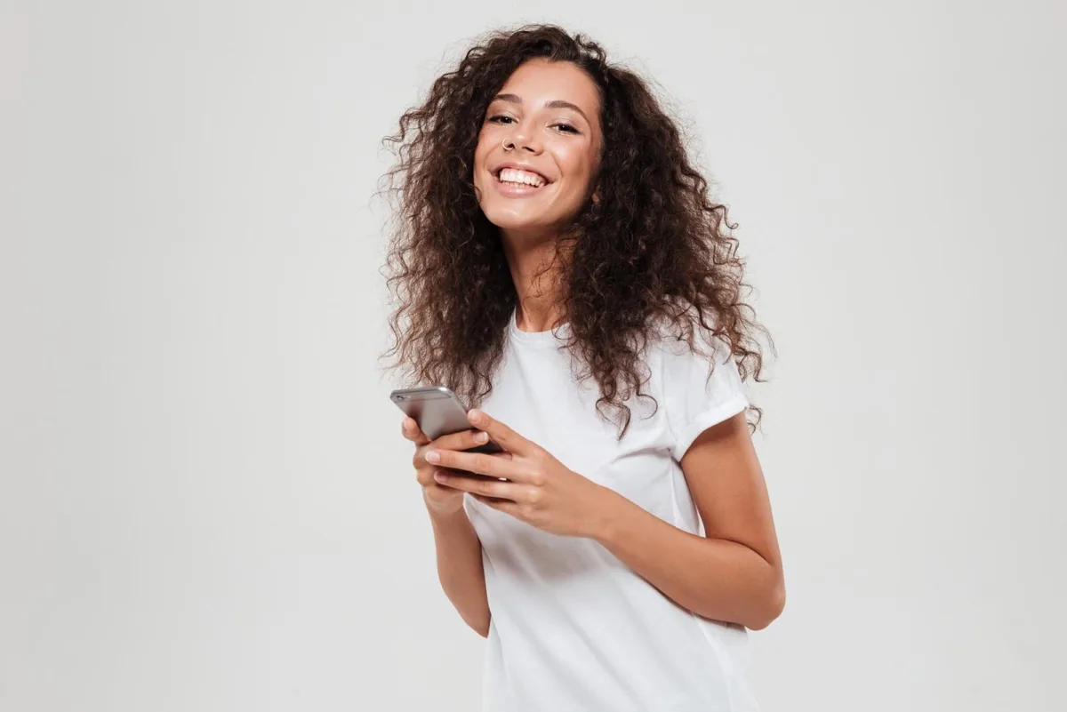 Mulher sorridente segurando o celular, representando o cliente que voltou a ter o nome limpo